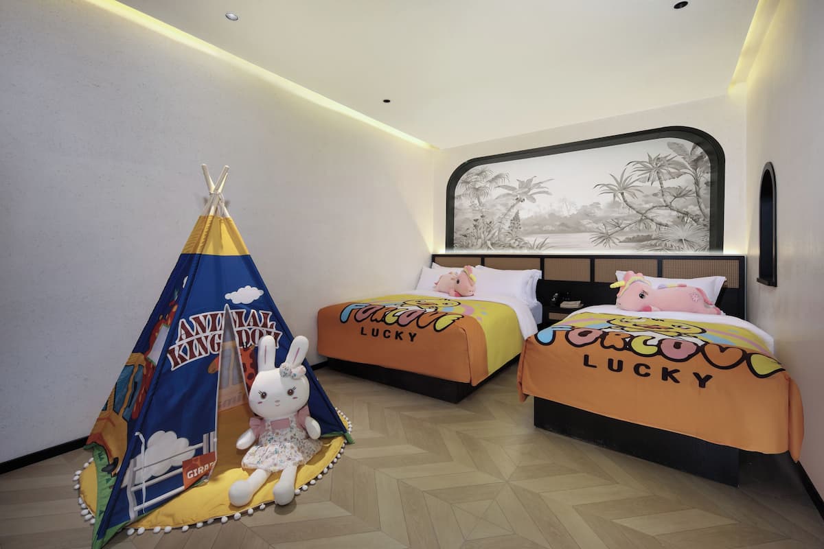 A hotel room with two beds, each with a 'Lucky' themed bedspread, a tent-like play area with a rabbit plush toy, and a wall mural.