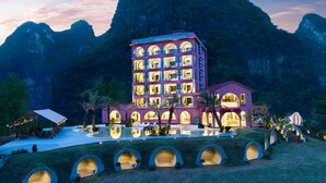 A multi-story hotel with a pool and outdoor seating area, surrounded by mountains. - Yangshuo Norton Manor Resort (Guilin)