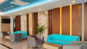 A modern lobby with a blue ceiling, a large TV, and a seating area with grey and turquoise sofas. - Front One Luxe Hotel Solo (Surakarta)