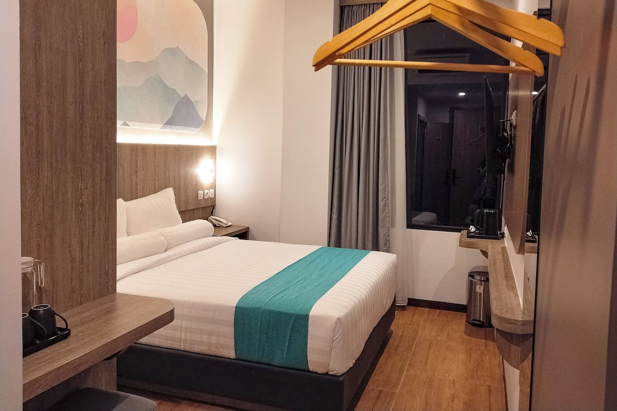 A hotel room with a bed, bedside table, lamp, and a window with curtains.