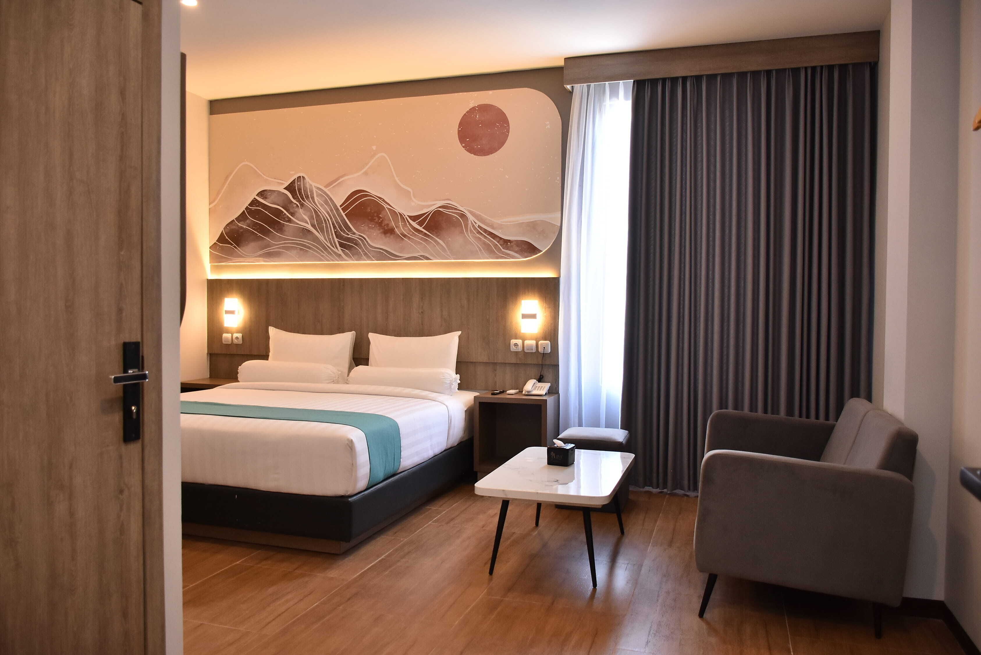 A hotel room with a bed, bedside table, chair, and a wall-mounted artwork.