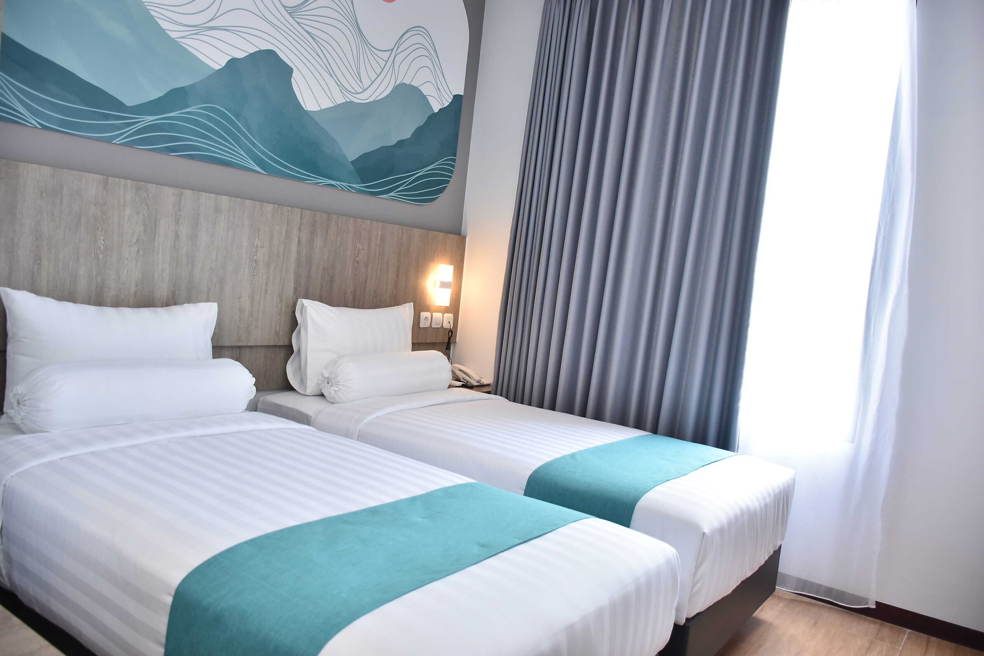 Une chambre d’hôtel avec deux lits, une tête de lit en bois, une fresque murale, une table de chevet avec un téléphone et une fenêtre avec des rideaux.