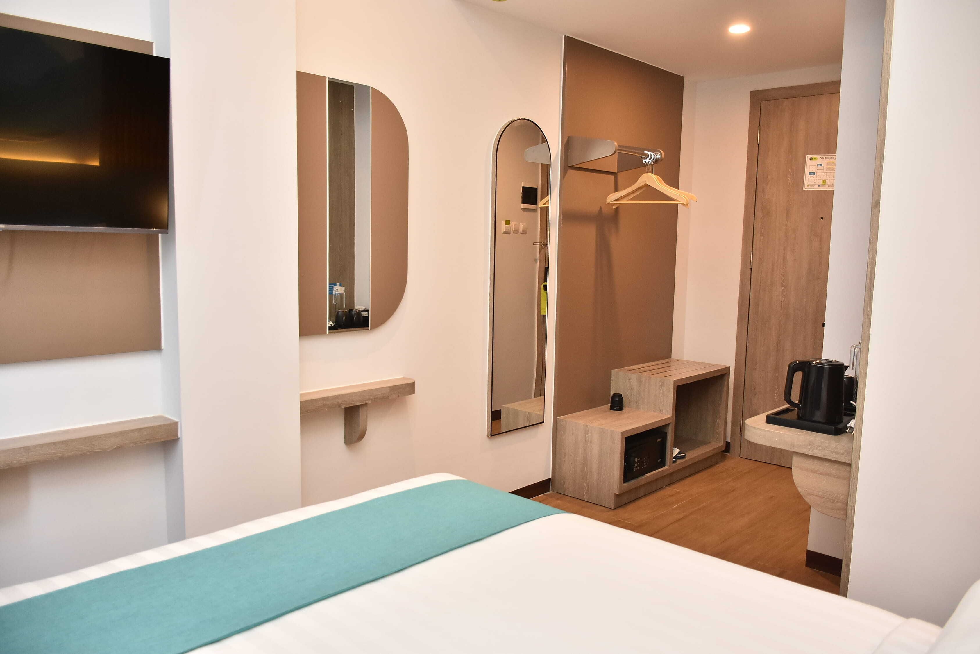 A hotel room with a bed, a TV, a mirror, a small wooden cabinet, a coffee maker, and a shower area.
