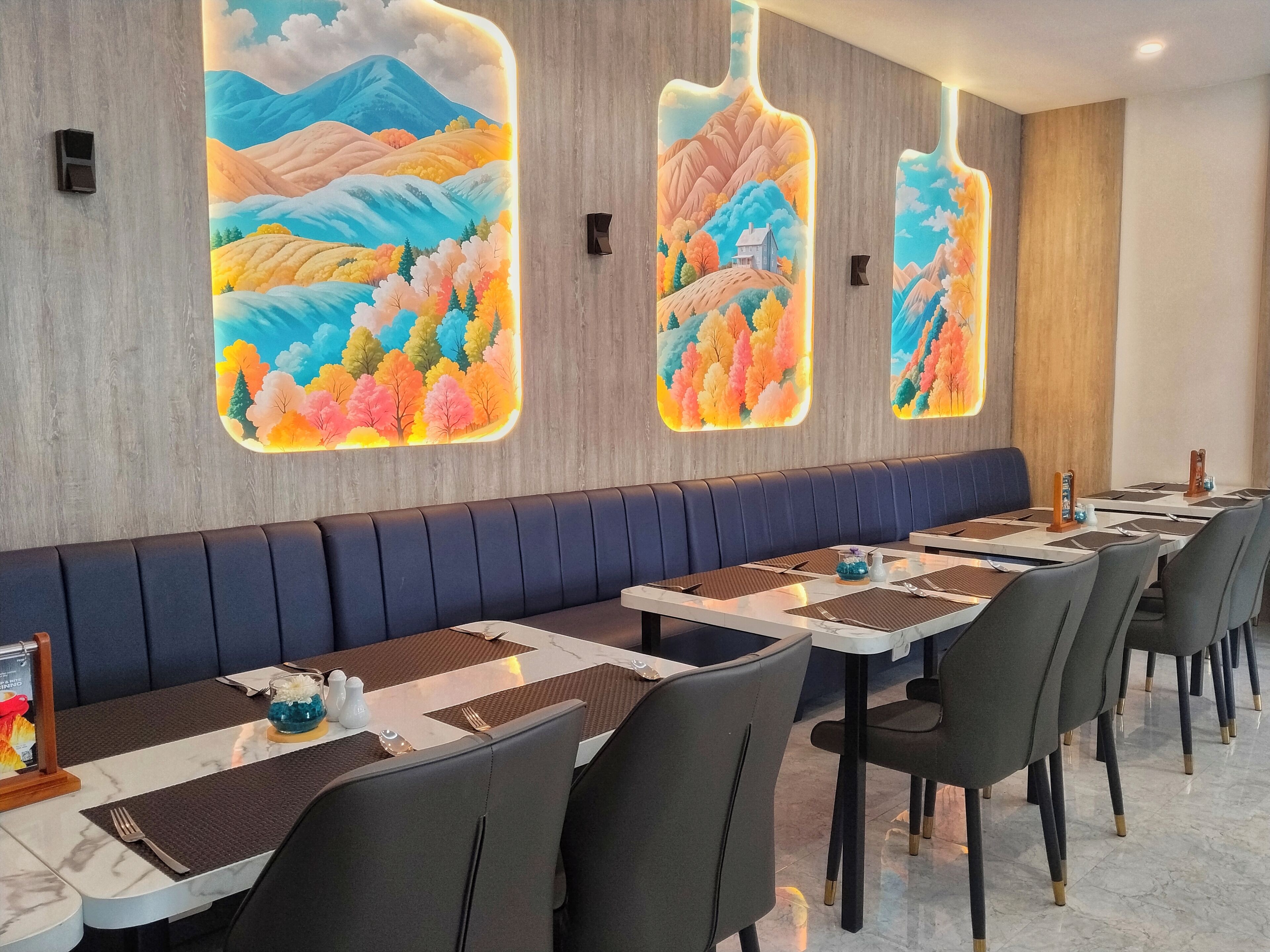 Un ristorante con un lungo bancone, sedute imbottite e grandi opere d'arte a parete raffiguranti paesaggi.