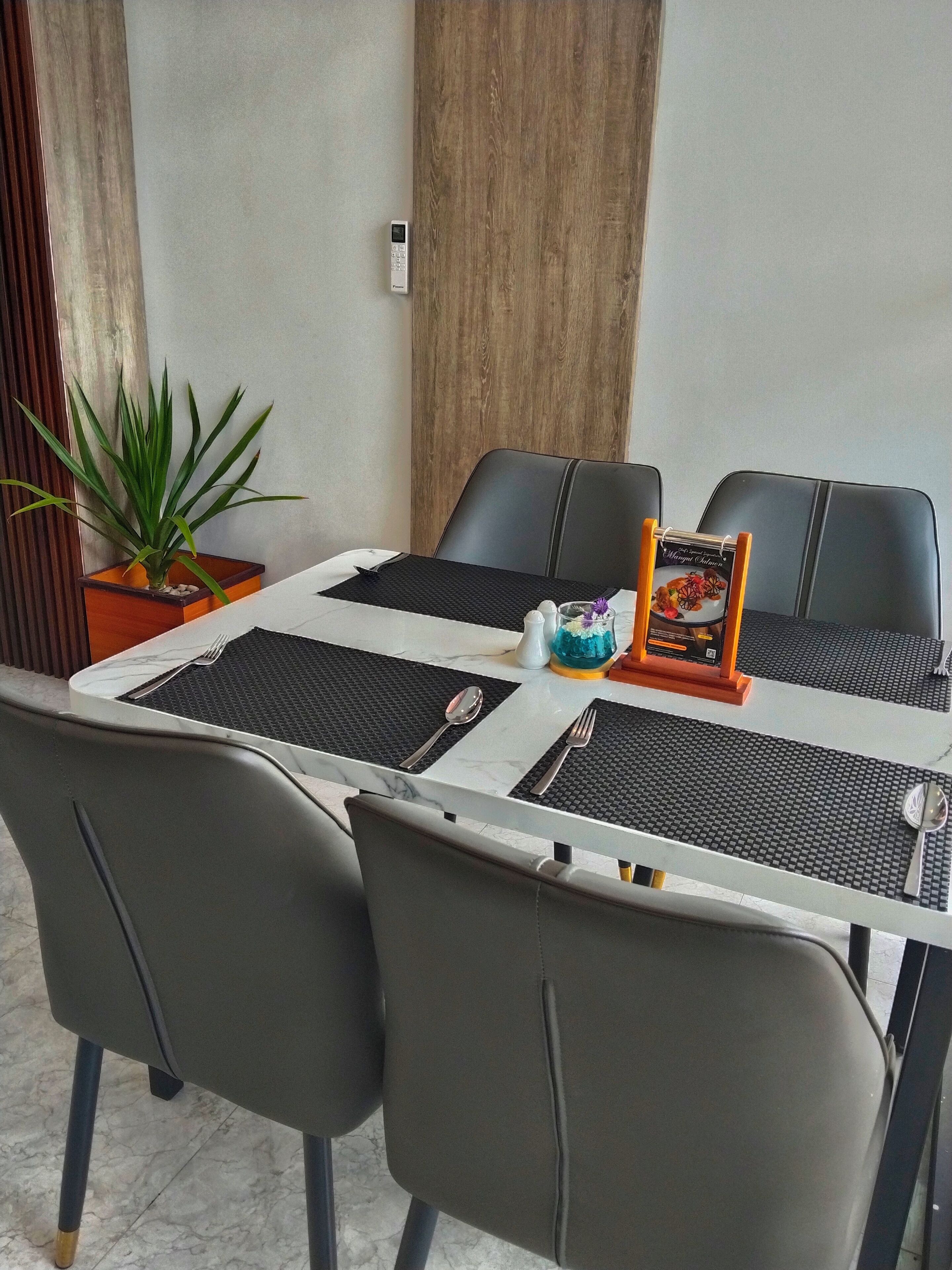 A dining area with a table set for four, black chairs, a potted plant, and a menu stand.