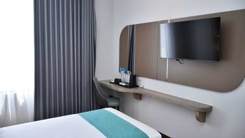 Ein Hotelzimmer mit Bett, Schreibtisch, Flachbildfernseher, Spiegel und einem Fenster mit Vorhängen.