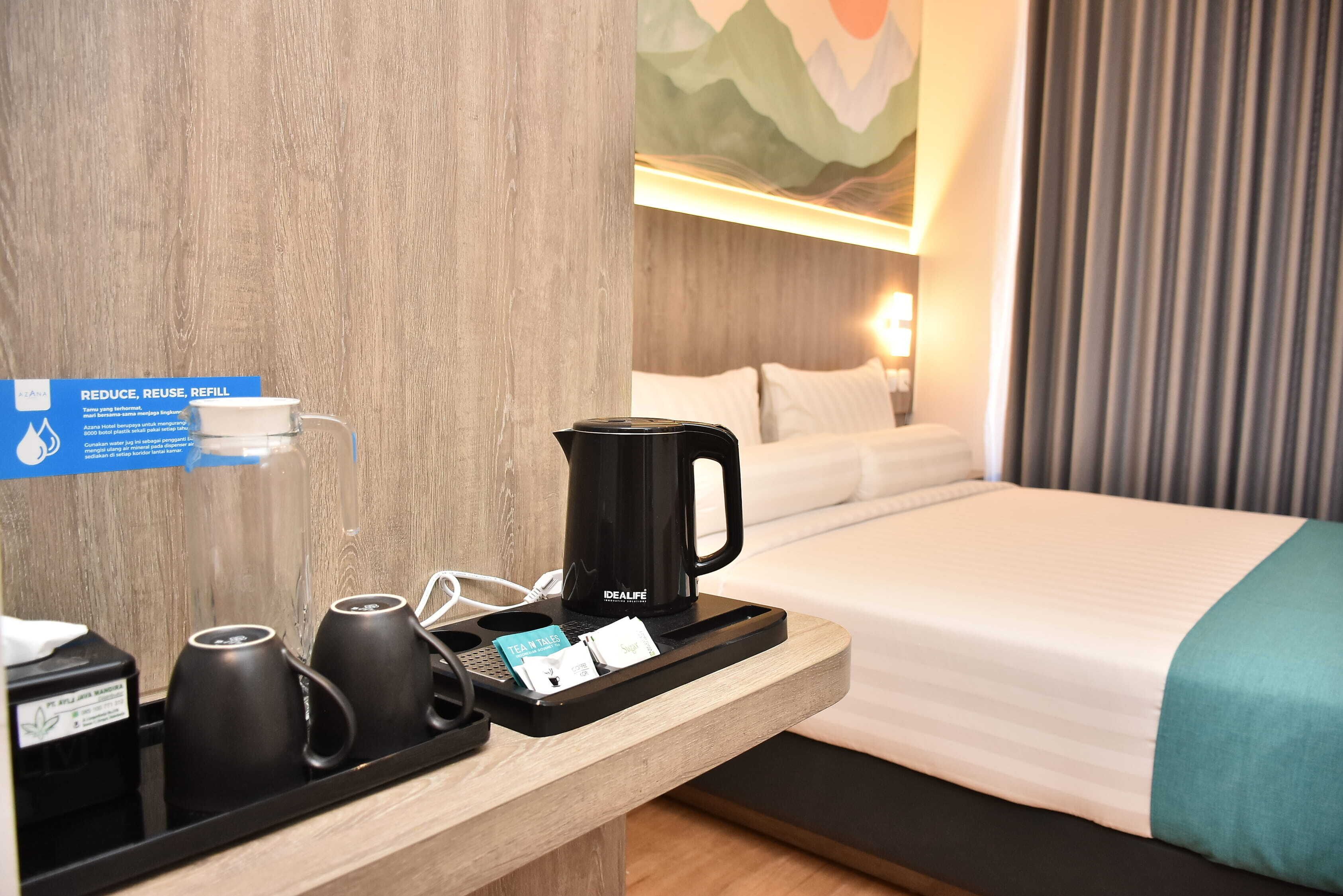 Habitación de hotel con una cama, una mesita de noche con hervidor, tazas y una bandeja con una bolsita de té y una tarjeta.