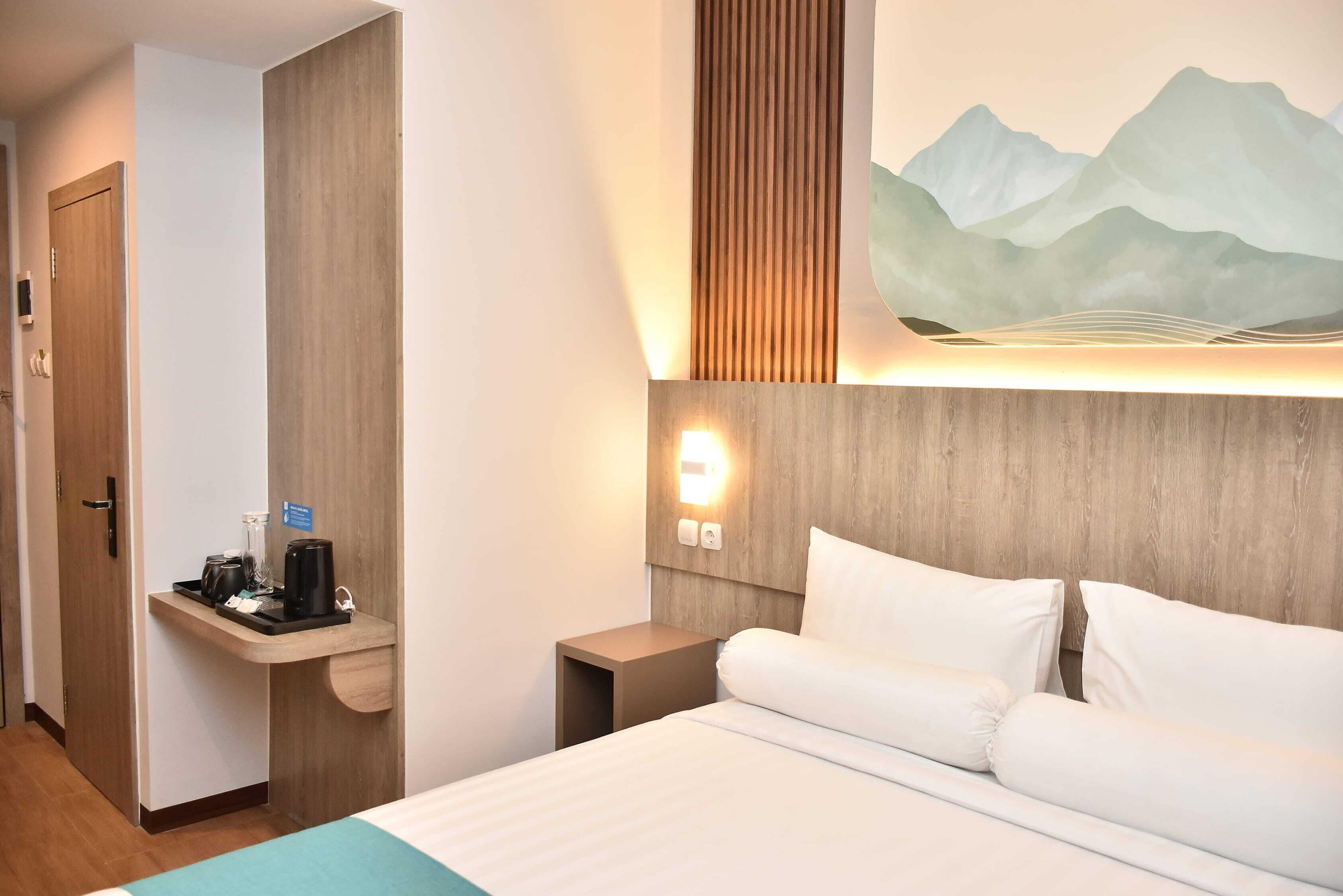 A hotel room with a bed, bedside table, and a wall-mounted light.