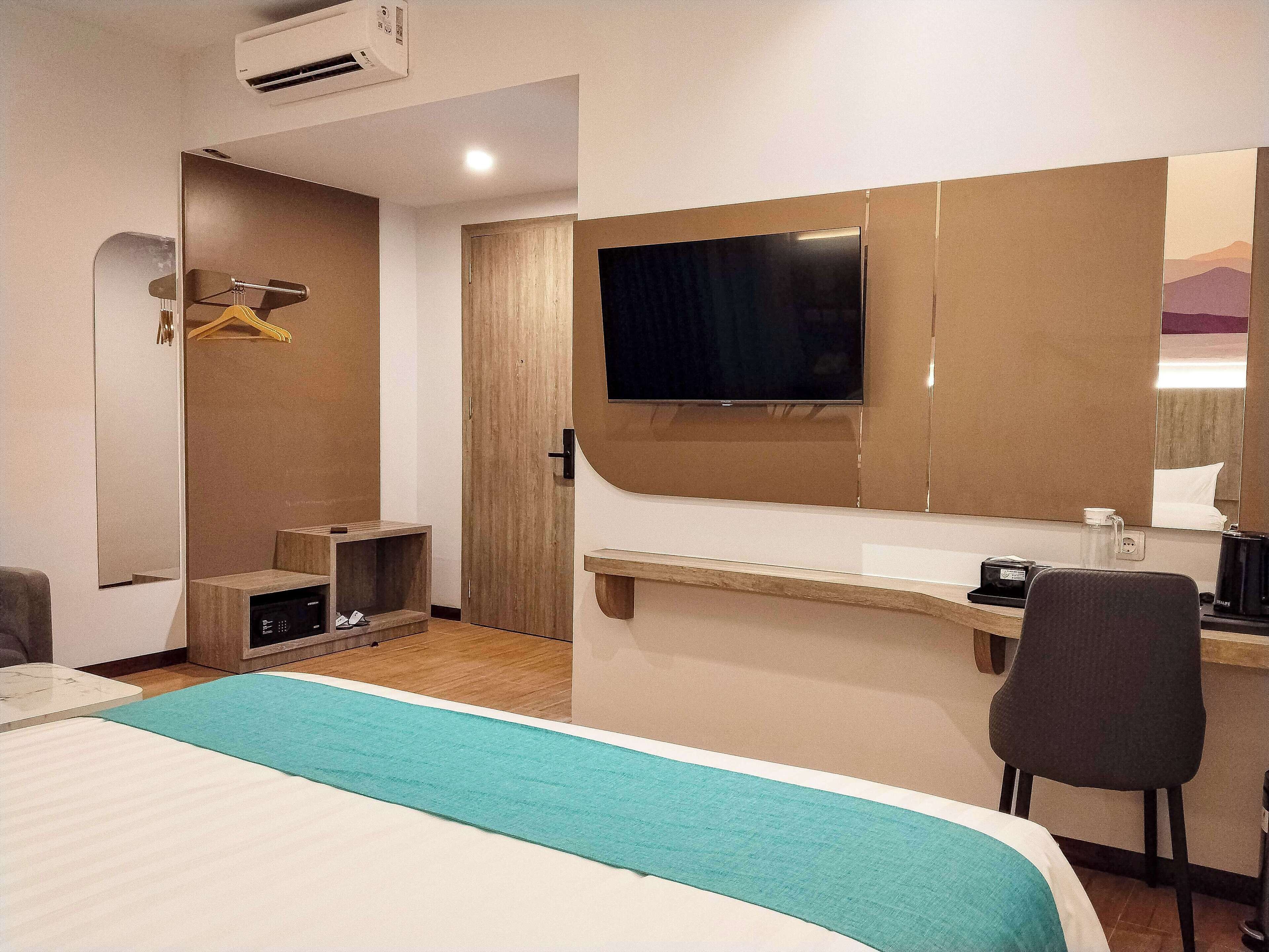 A hotel room with a bed, a desk, a chair, a TV, and a wardrobe.