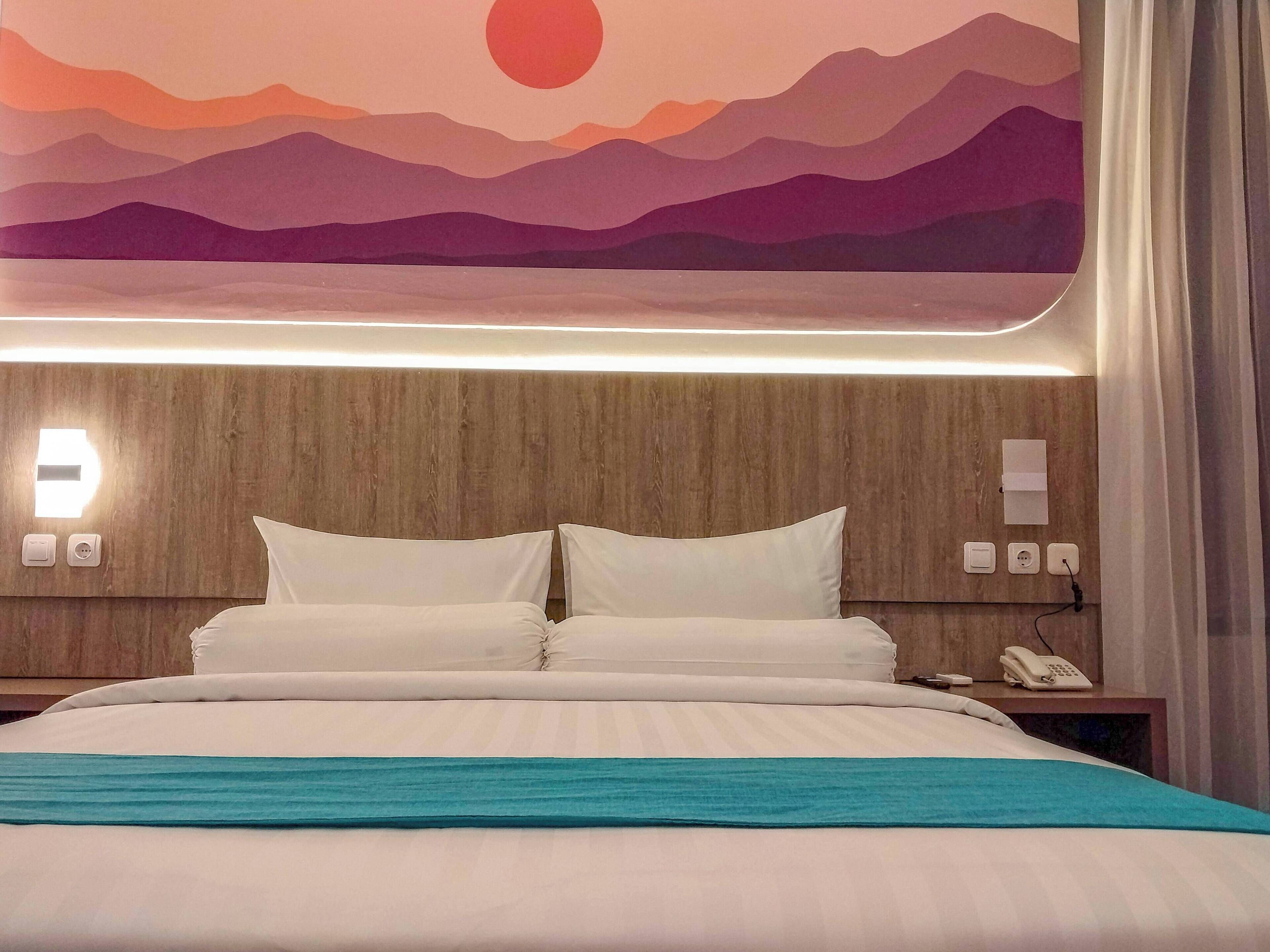 A hotel room with a bed, a nightstand with a phone, and a wall-mounted light.