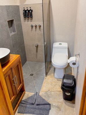 A bathroom with a shower, toilet, sink, and storage cabinet.