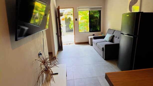 A modern living room with a flat-screen TV, a sofa, a dining table, and a refrigerator. - Jacaranda (Puerto Viejo de Talamanca)