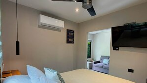 A bedroom with a bed, a ceiling fan, an air conditioning unit, a mounted TV, and a wall-mounted sign. - Jacaranda (Puerto Viejo de Talamanca)