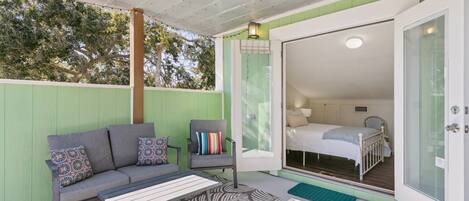 Un área de estar al aire libre acogedora, con un sofá y sillones, alfombra estampada y vista a un dormitorio con cama y ventana.