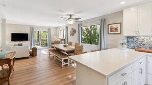 A modern kitchen with a large island, dining area, and a television in a living room.
