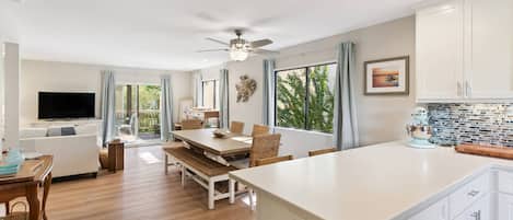 A modern kitchen with a large island, dining area, and a television in a living room.