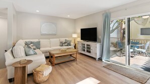A living room with a sofa, coffee table, TV, and a glass door leading to an outdoor seating area.