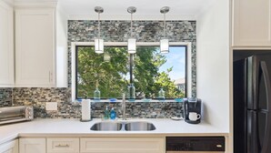 A modern kitchen with a stone backsplash, a double sink, a coffee maker, and a dishwasher.