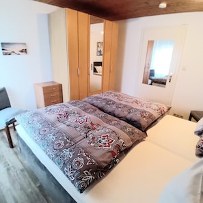 A bedroom with a bed, a wardrobe, a mirror, and a small table.
