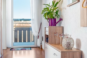 Ein Zimmer mit einem Holzkabinett, einer violetten Gießkanne, einem Topfpflanzen und dekorativen Glasobjekten.