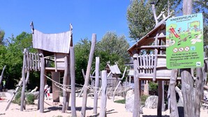 Un parque infantil con estructuras de madera y un cartel que indica que es una zona de juegos para niños.