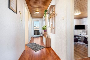 Un pasillo con suelo de madera, una alfombra, una planta y un aplique en la pared.