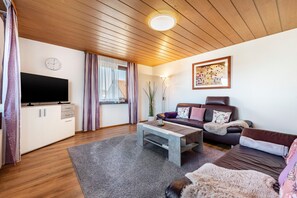 Un salon moderne avec un téléviseur à écran plat, un ensemble de canapés, une table basse et un tableau accroché au mur.