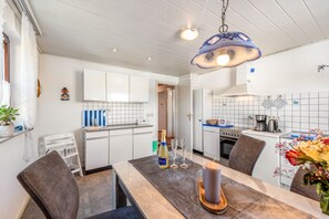 Une cuisine moderne avec des meubles blancs, un coin repas doté d’une table en bois et un luminaire suspendu.