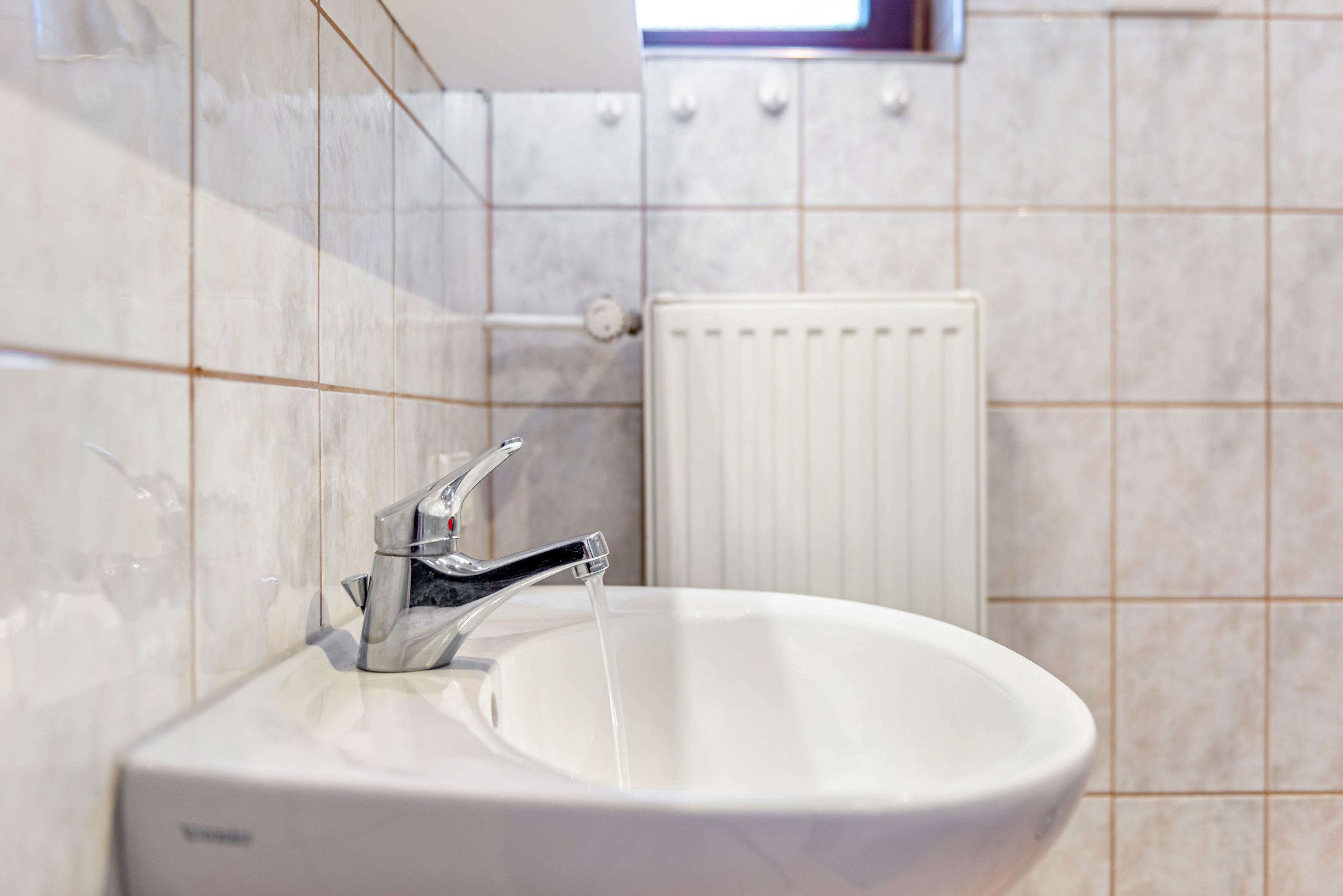 Une salle de bain avec un lavabo blanc, un robinet chromé et un radiateur blanc.