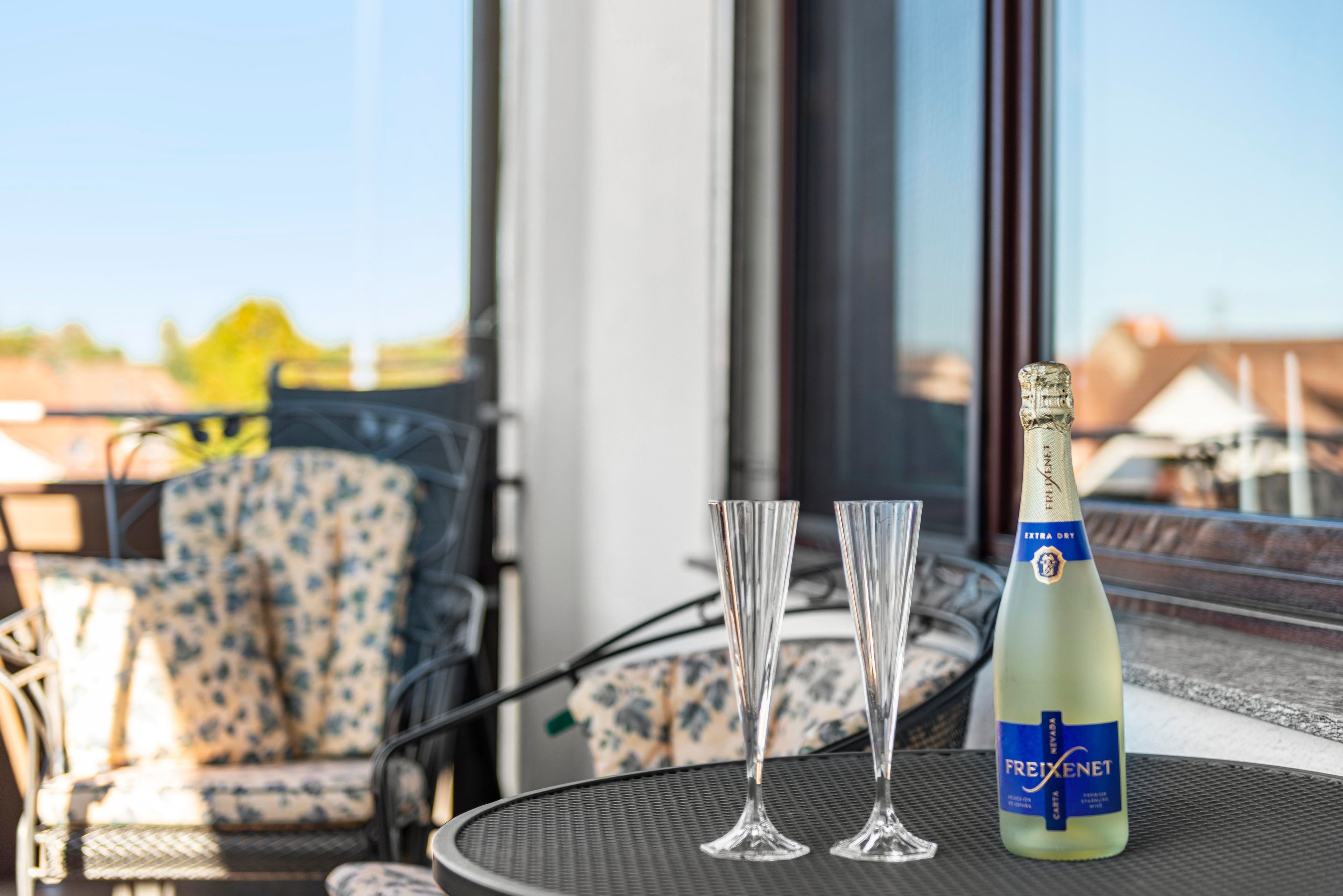 A table with a bottle of Freixenet champagne and two glasses on a balcony with a view.