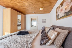 A bedroom with a wooden ceiling, a bed with multiple pillows, a large mirror, and a painting of roses on the wall.