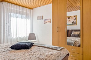 Une chambre à coucher avec un lit, une armoire, une chaise et une fenêtre avec des rideaux.