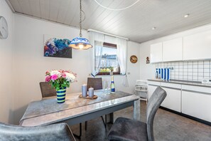 Eine moderne Küche mit weißen Schränken, einem Esstisch mit Stühlen, einem Blumenstrauß und einer Pendelleuchte.
