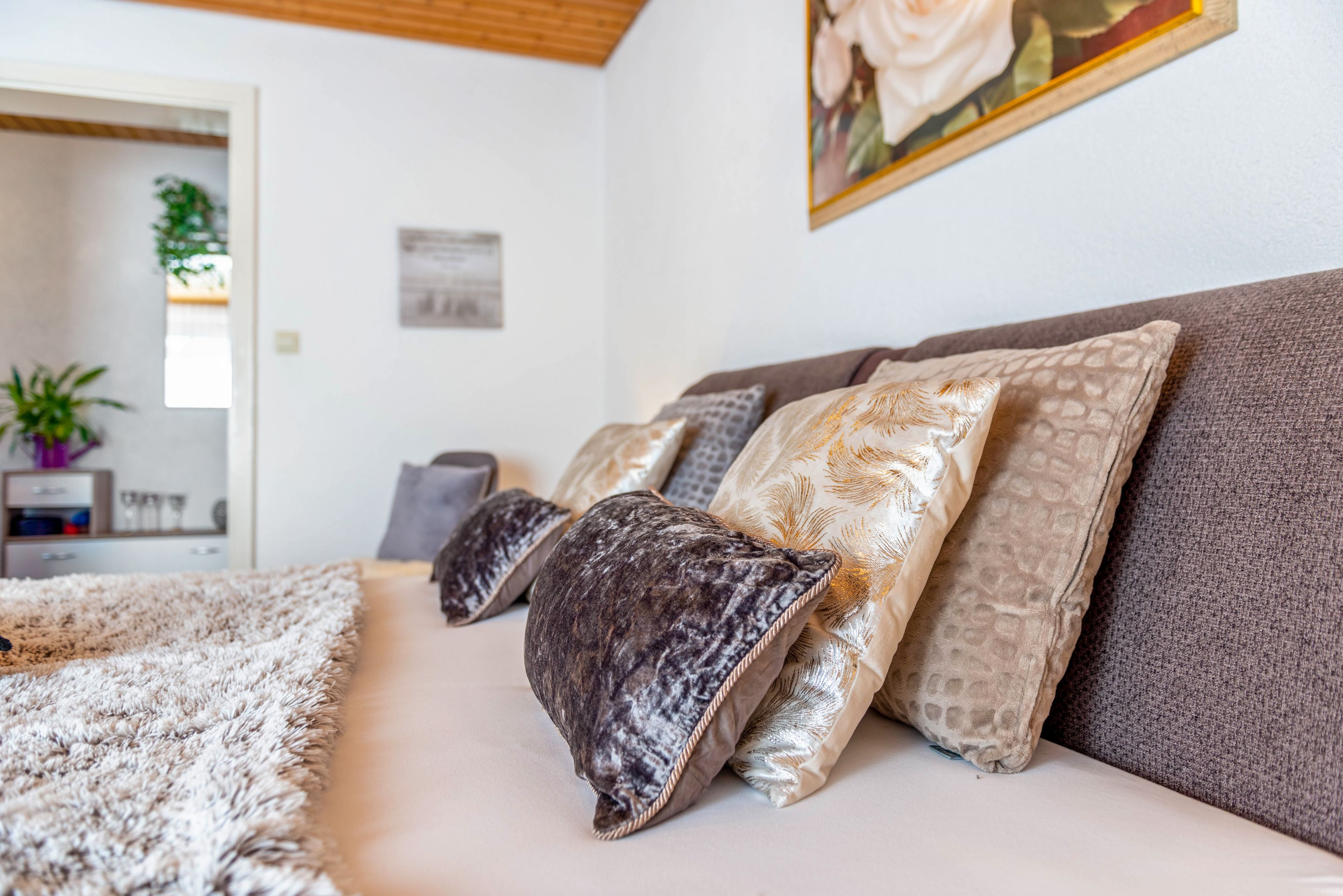 A living room with a sofa, multiple cushions, a fluffy rug, and a painting on the wall.