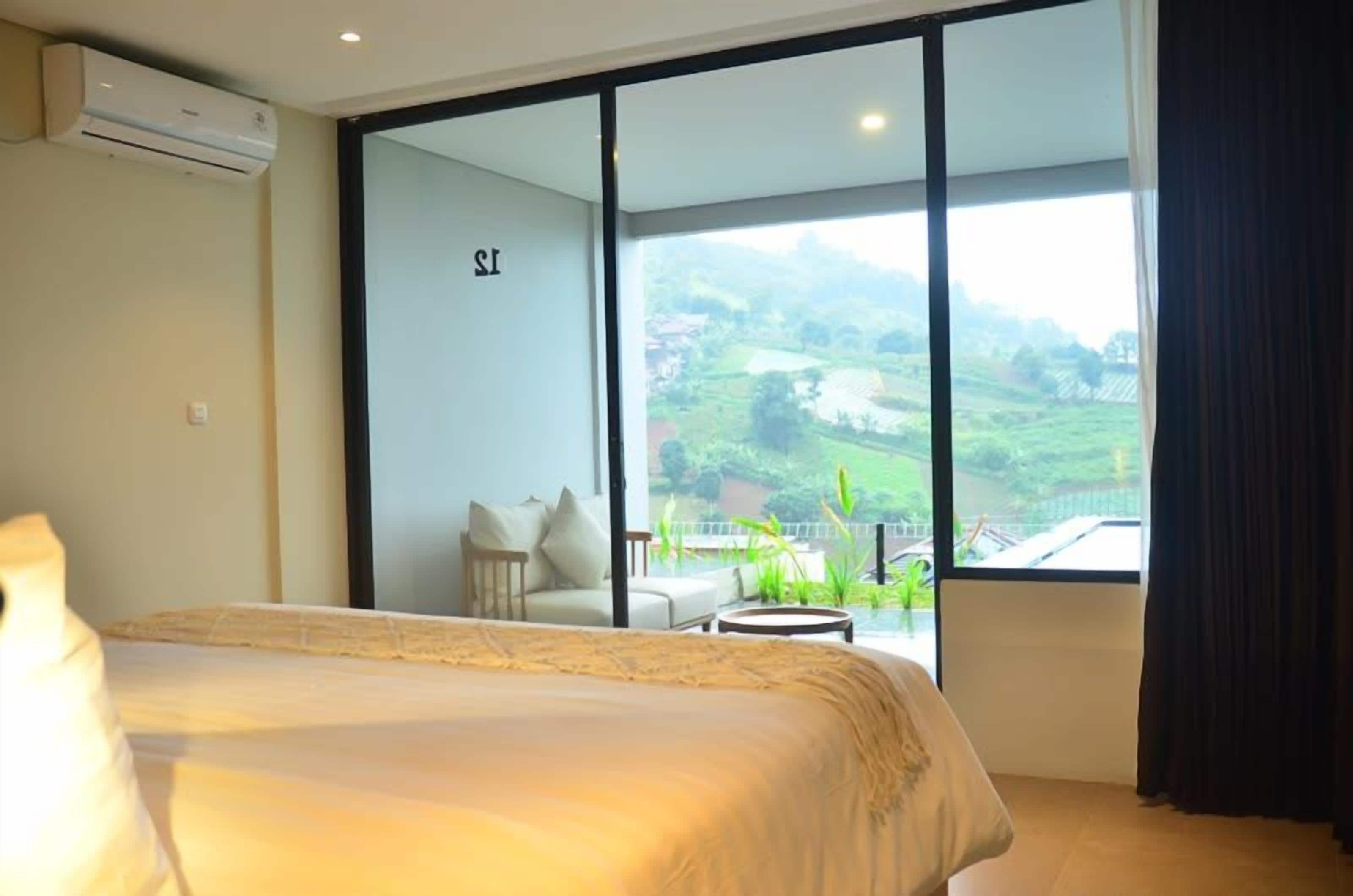 Habitación de hotel con una cama grande, una mesita y vista a un paisaje exuberante a través de una puerta corredera.