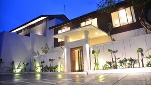 Un edificio moderno con un ingresso ben illuminato, un portico coperto e un'area verde con piante.