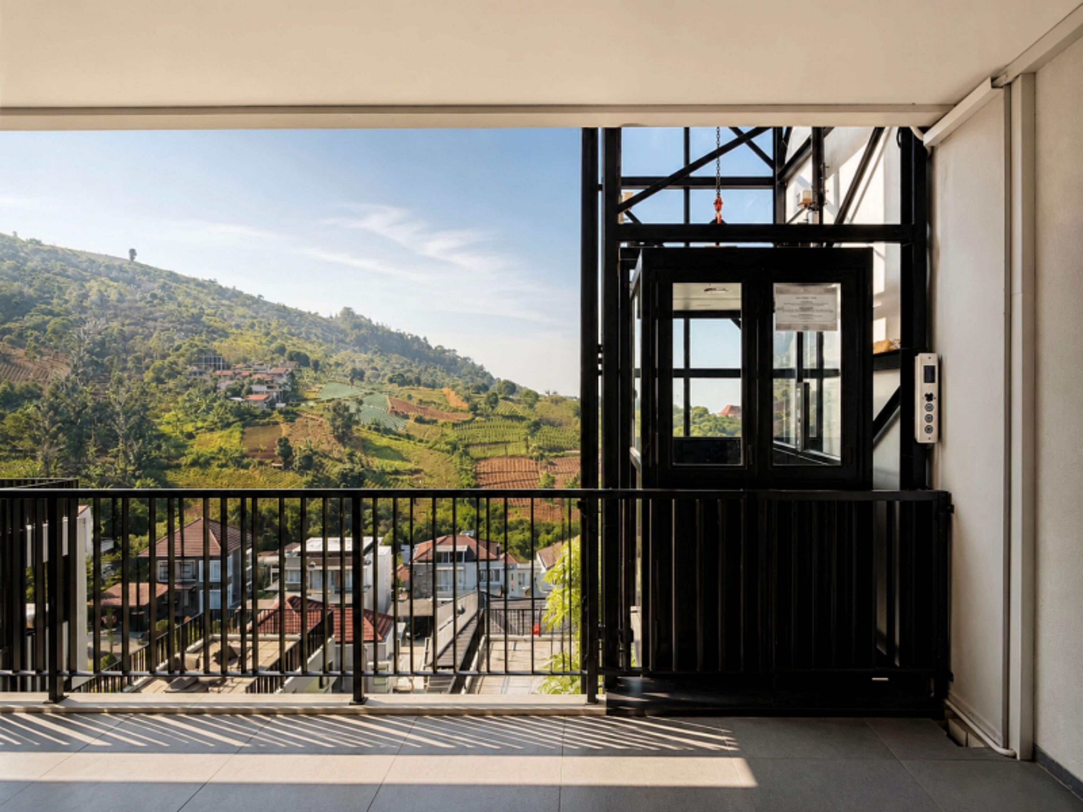 Un balcón con vistas a un paisaje montañoso, un portón negro y un cielo despejado.