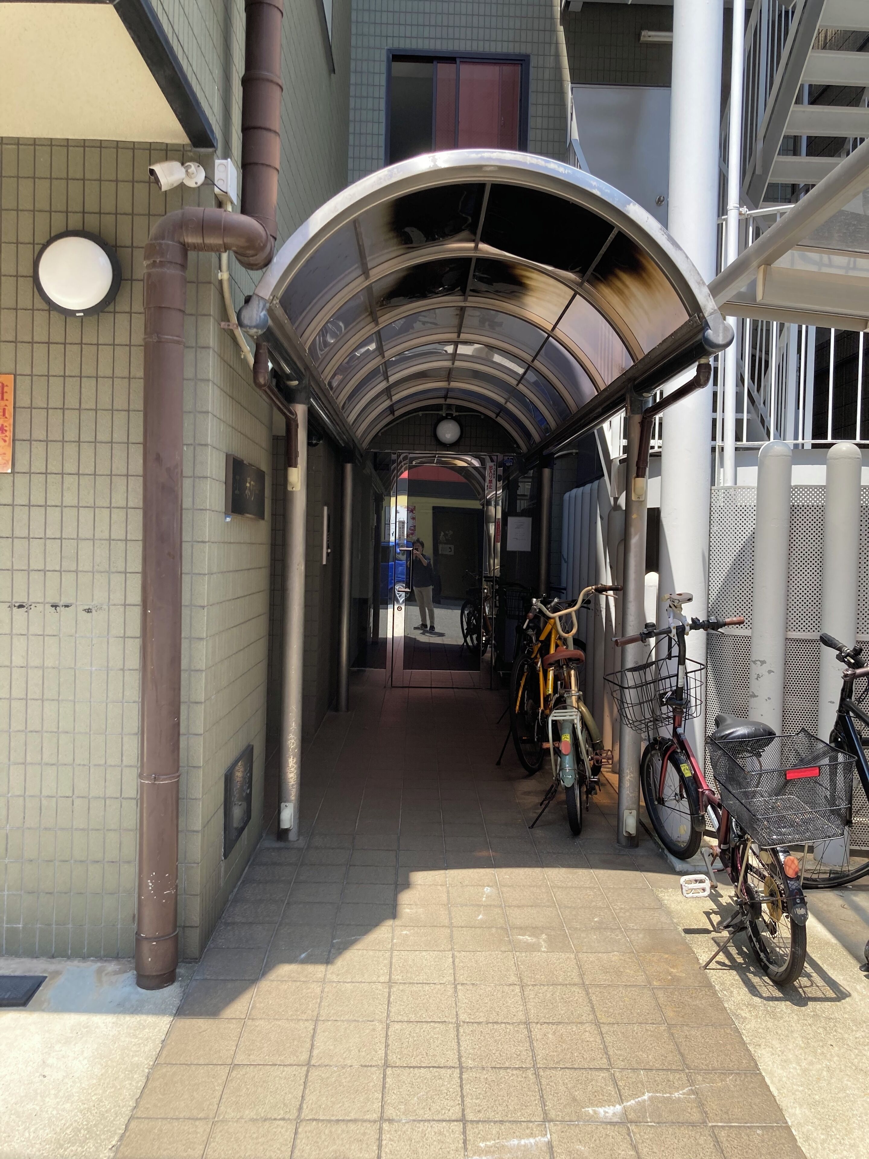 A covered walkway with bicycles parked on the side, a tiled wall, and a building entrance.