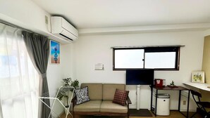 Ein kleiner Wohnbereich mit einer Couch, einem Tisch, einem Stuhl, einem Fernseher und einem Mülleimer.