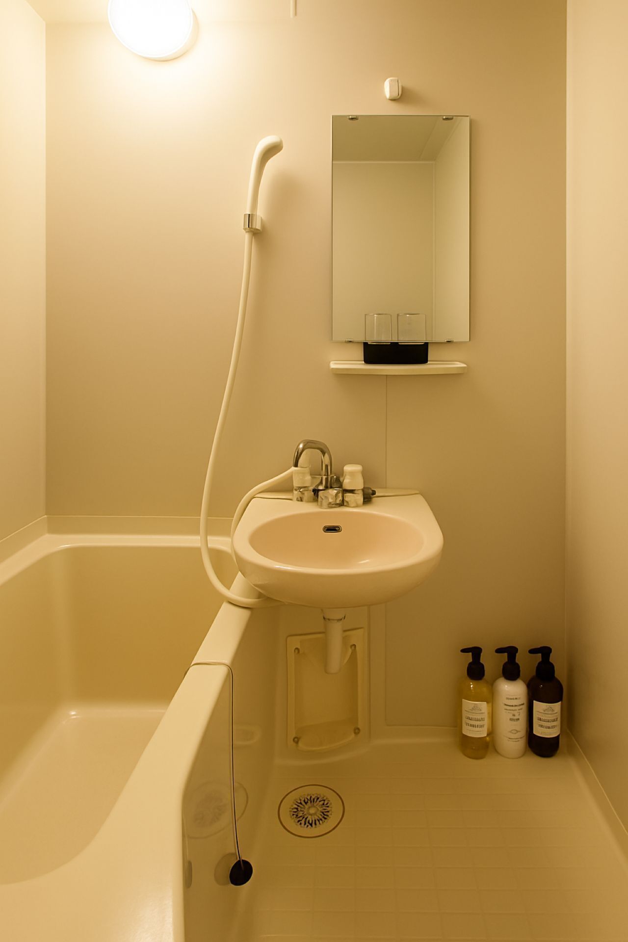 Ein Badezimmer mit einer Badewanne, einem Waschbecken und einem Spiegel darüber. Auf dem Waschtischrand stehen drei Kosmetikflaschen.