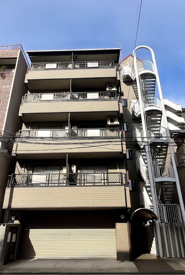 A multi-story residential building with balconies, air conditioning units, and a garage door. - Casa G.S. Ebisucho (Osaka)