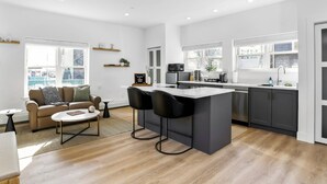 A modern kitchen with a central island, bar stools, and a dining area with a sofa and coffee table. - Modern Studio, Harbor Point #1– Walk to Train, Restaurants, City + Shore (Stamford)