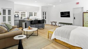 A modern hotel room with a bed, a sofa, a small dining table, a kitchen area, and an exit sign. - Modern Studio, Harbor Point #1– Walk to Train, Restaurants, City + Shore (Stamford)