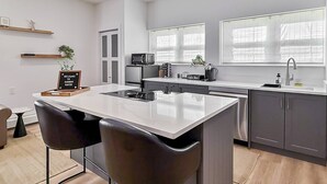 A modern kitchen with a central island, bar stools, a microwave, a coffee machine, and a sink. - Modern Studio, Harbor Point #1– Walk to Train, Restaurants, City + Shore (Stamford)