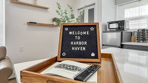 A modern kitchen with a microwave, a Samsung remote, and a wooden tray with a welcome sign. - Modern Studio, Harbor Point #1– Walk to Train, Restaurants, City + Shore (Stamford)