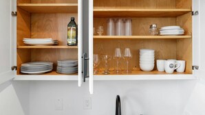 Un armario de cocina con estantes de madera que contienen platos, vasos y una botella de aceite de oliva.