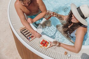 A couple in a hot tub with a bottle of champagne and a plate of strawberries.
