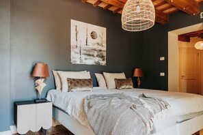 A bedroom with a bed, two bedside tables, a hanging light fixture, and a painting on the wall.