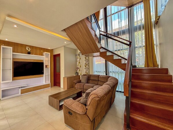 Una sala de estar moderna con un televisor de pantalla plana grande, un sofá, una mesa de centro y una escalera que sube a un nivel superior.