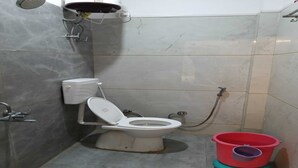 Ein kleines Badezimmer mit Toilette, Dusche und einem Eimer.